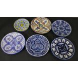 A collection of six majolica ceramic hand painted chargers, each with a different design, some