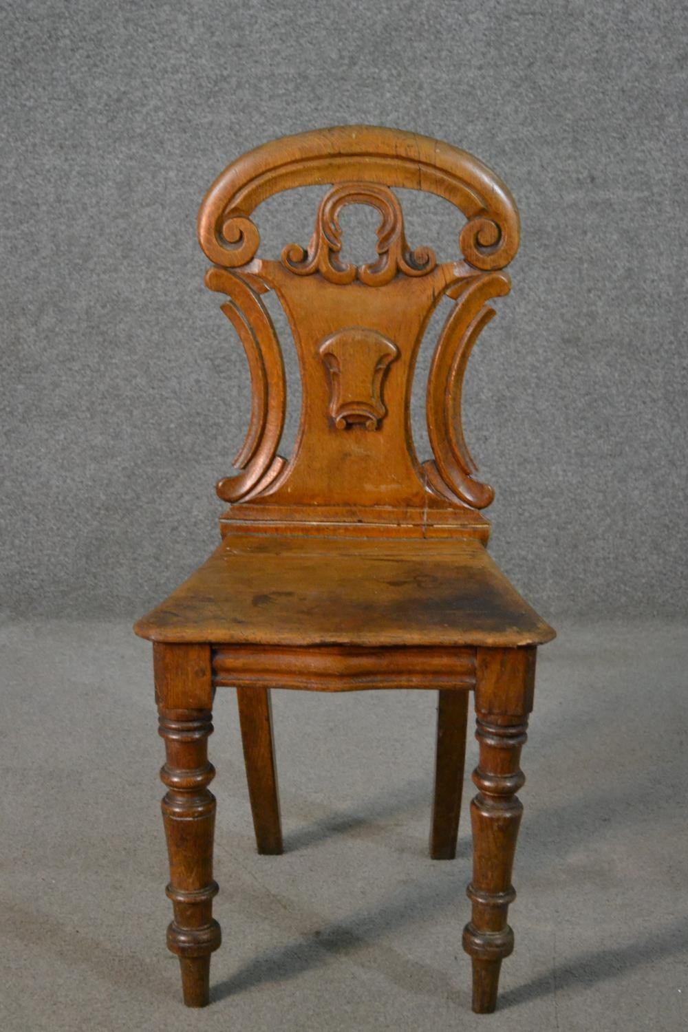 A Victorian oak hall chair, with a carved and pierced scrolling back, on turned legs.