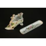 A 19th century hand painted porcelain slipper with relief cherub sitting upon it along with a