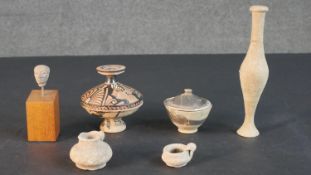 A collection of Roman and ancient Greek pottery, including a miniature clay head on a wooden base,