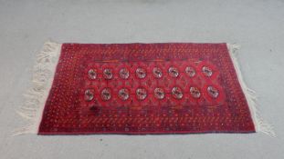 An Afghan rug with repeating gul motifs on a burgundy ground. L.125 W.78cm