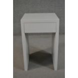 A contemporary white bedside table, of rectangular form with a single frieze drawer on end supports.