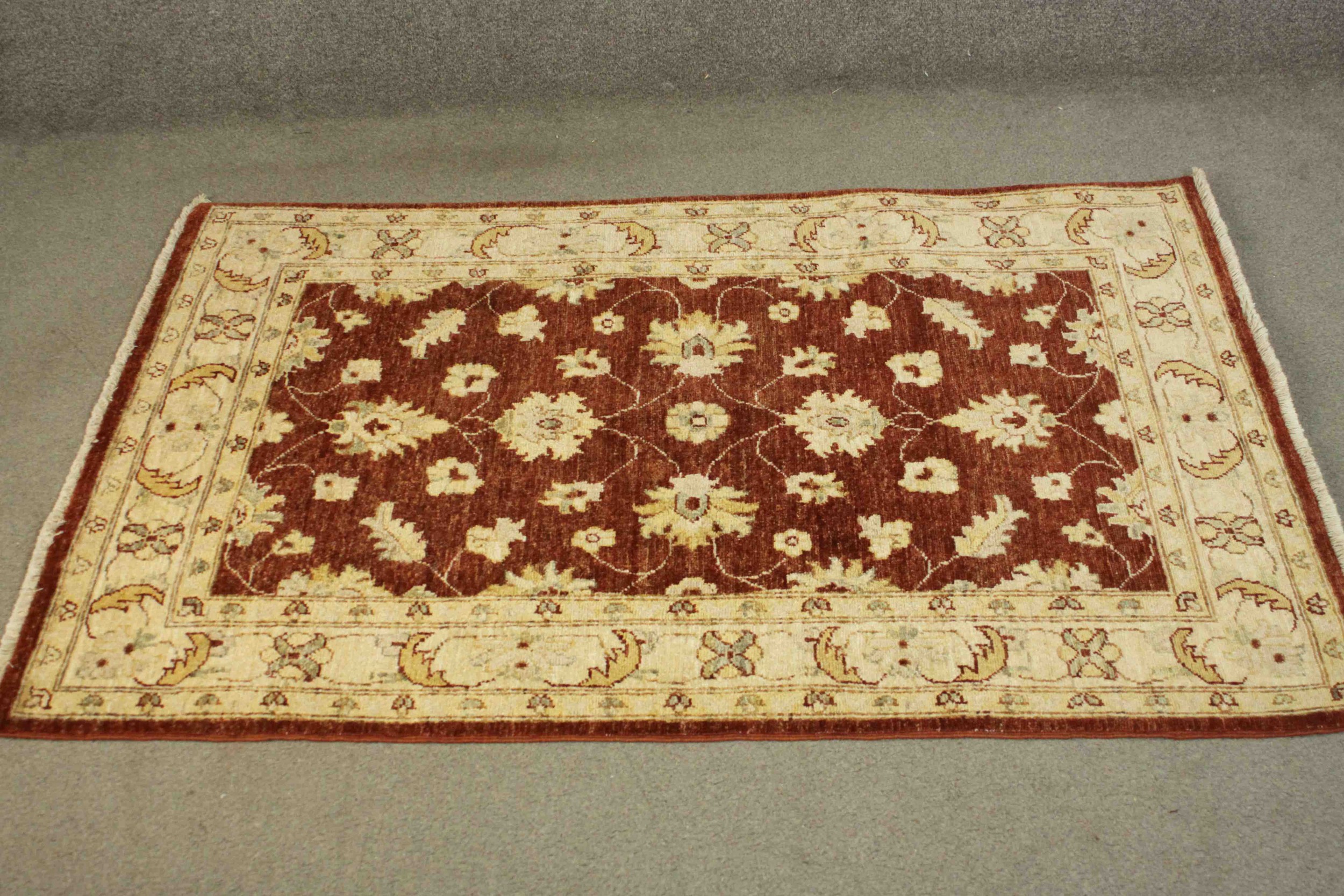 A Ziegler style rug with repeating foliate motifs on a burgundy field within serrated palm