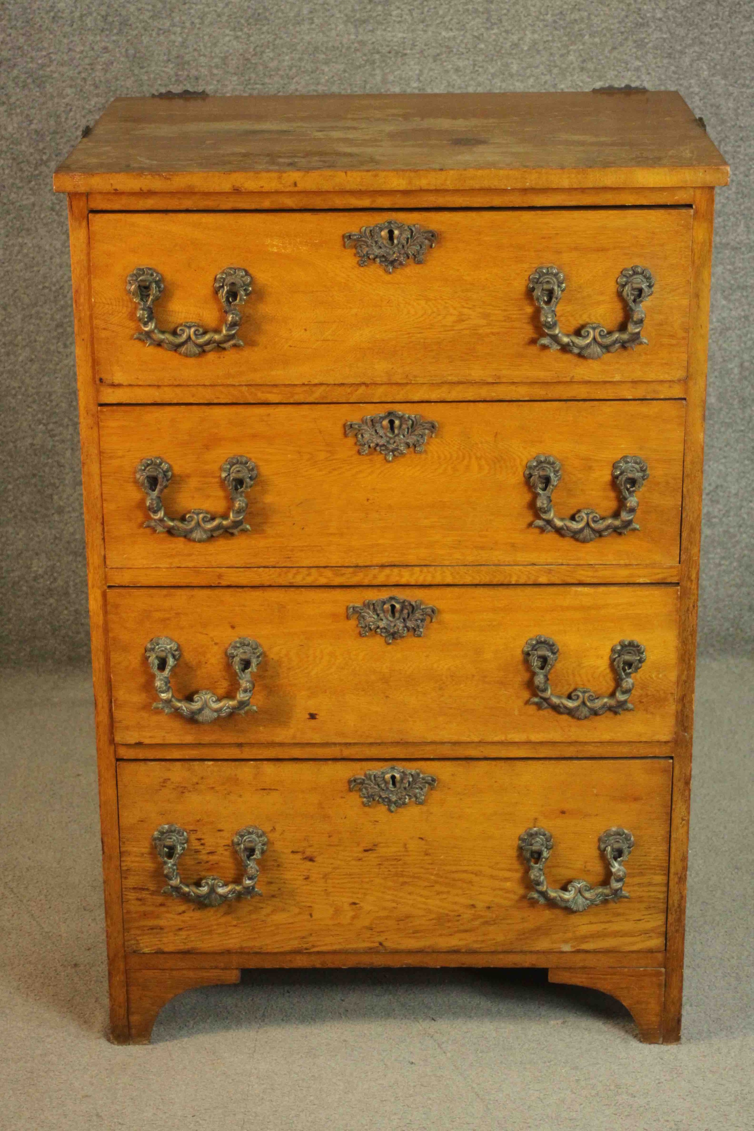 A late 19th/early 20th century oak chest of four long drawers with ornately cast bronze swing