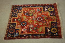 A Persian Belouch rug with stylised figural motifs across the madder ground within flowerhead