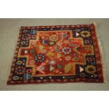 A Persian Belouch rug with stylised figural motifs across the madder ground within flowerhead