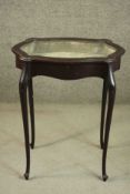 An early 20th century French mahogany bijouterie table, the glazed top of cartouche form enclosing a