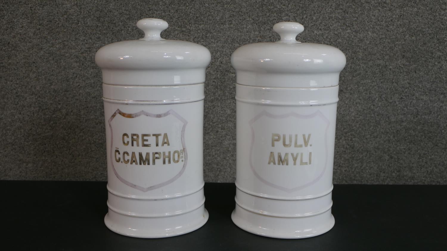 Two large 19th century white ceramic lidded apothecary jars, gilded Latin lettering with a shield