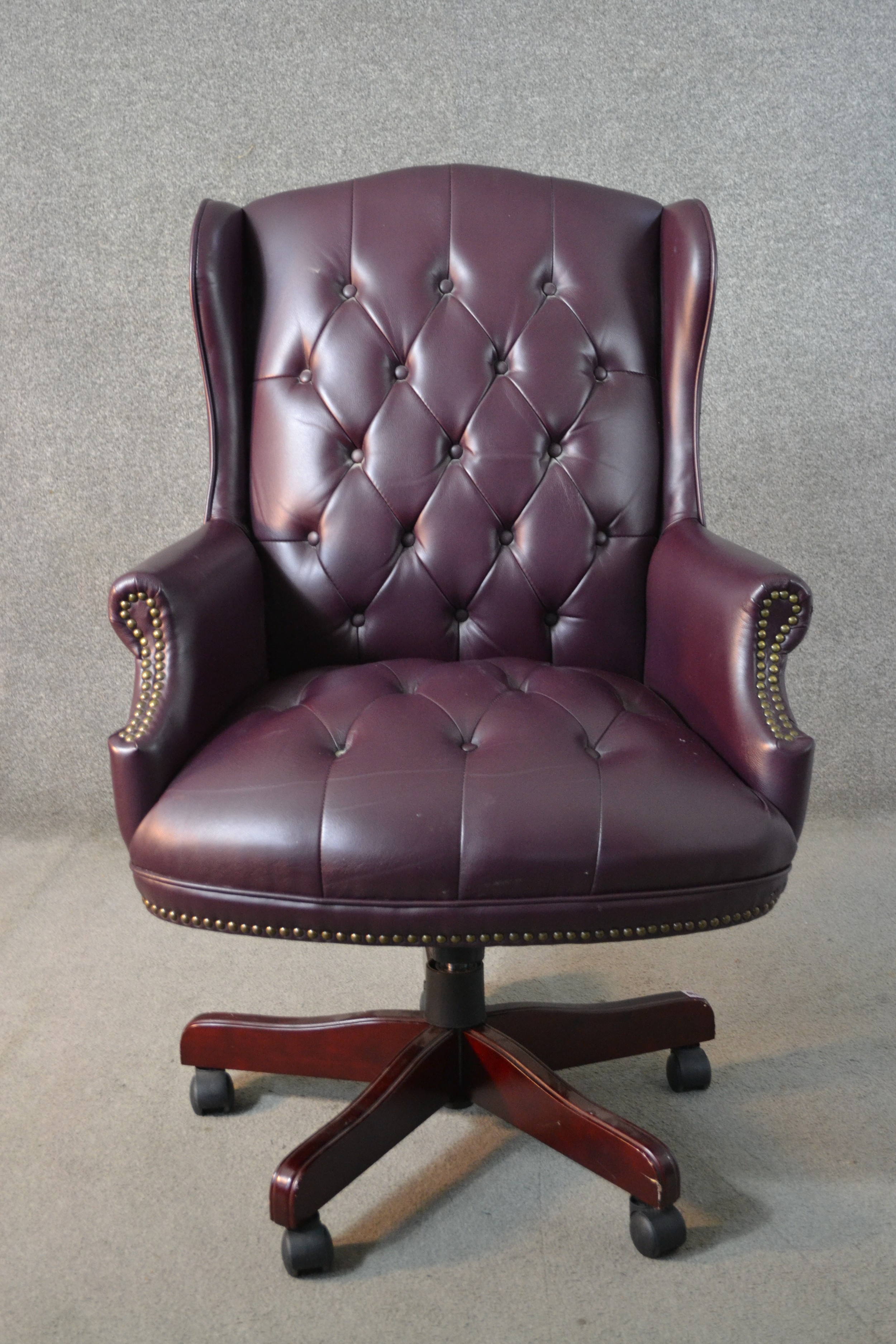 A 20th century wing back swivel office chair, upholstered in burgundy leather, with buttoned back