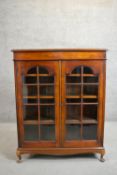 An early to mid-20th century fruitwood display cabinet, the two glazed doors enclosing shelves on