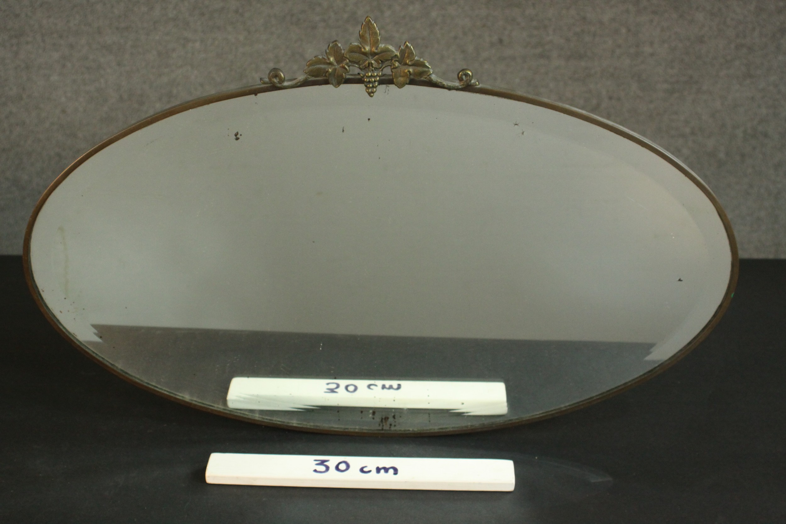 An early 20th century oval mirror in a brass frame and a vine crest. H.45 W.69cm. - Image 2 of 4