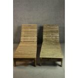 A pair of contemporary teak garden sun loungers of slatted form with adjustable back, on wheels. H.