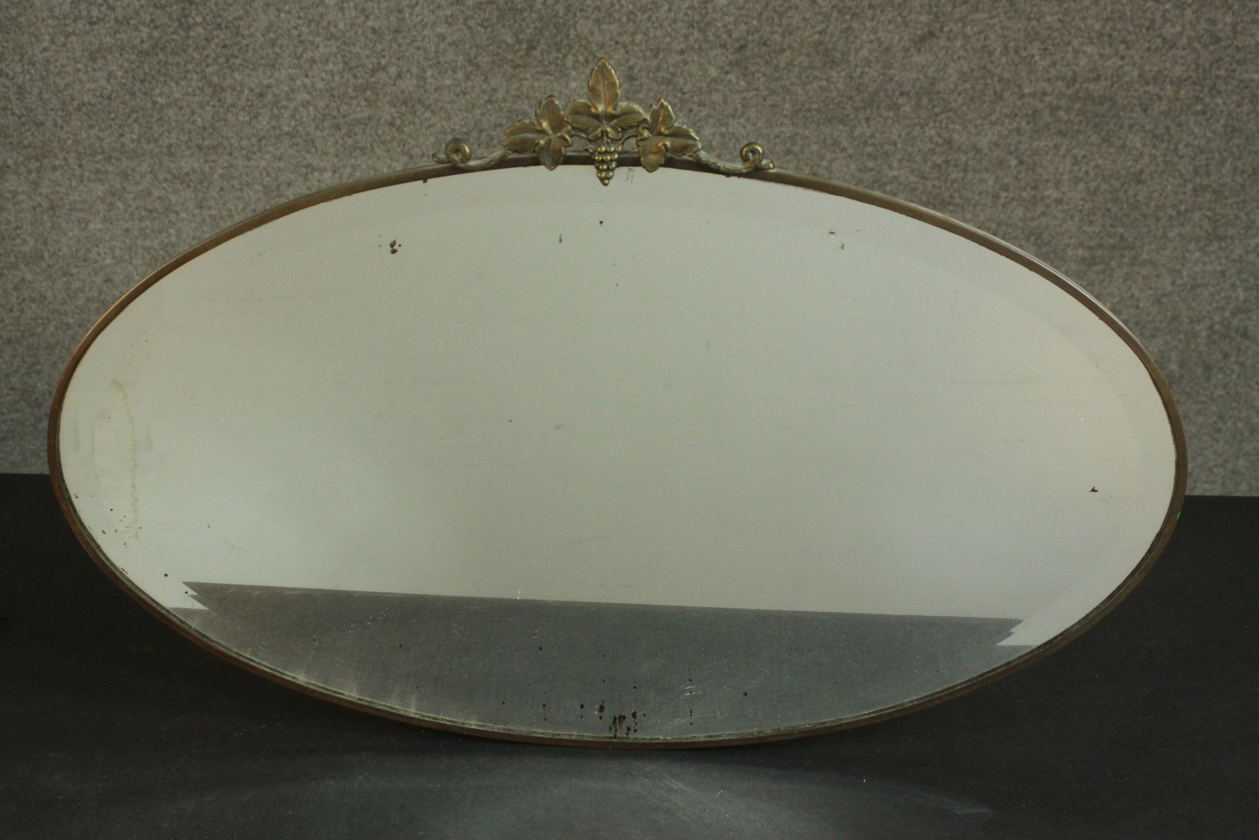 An early 20th century oval mirror in a brass frame and a vine crest. H.45 W.69cm.