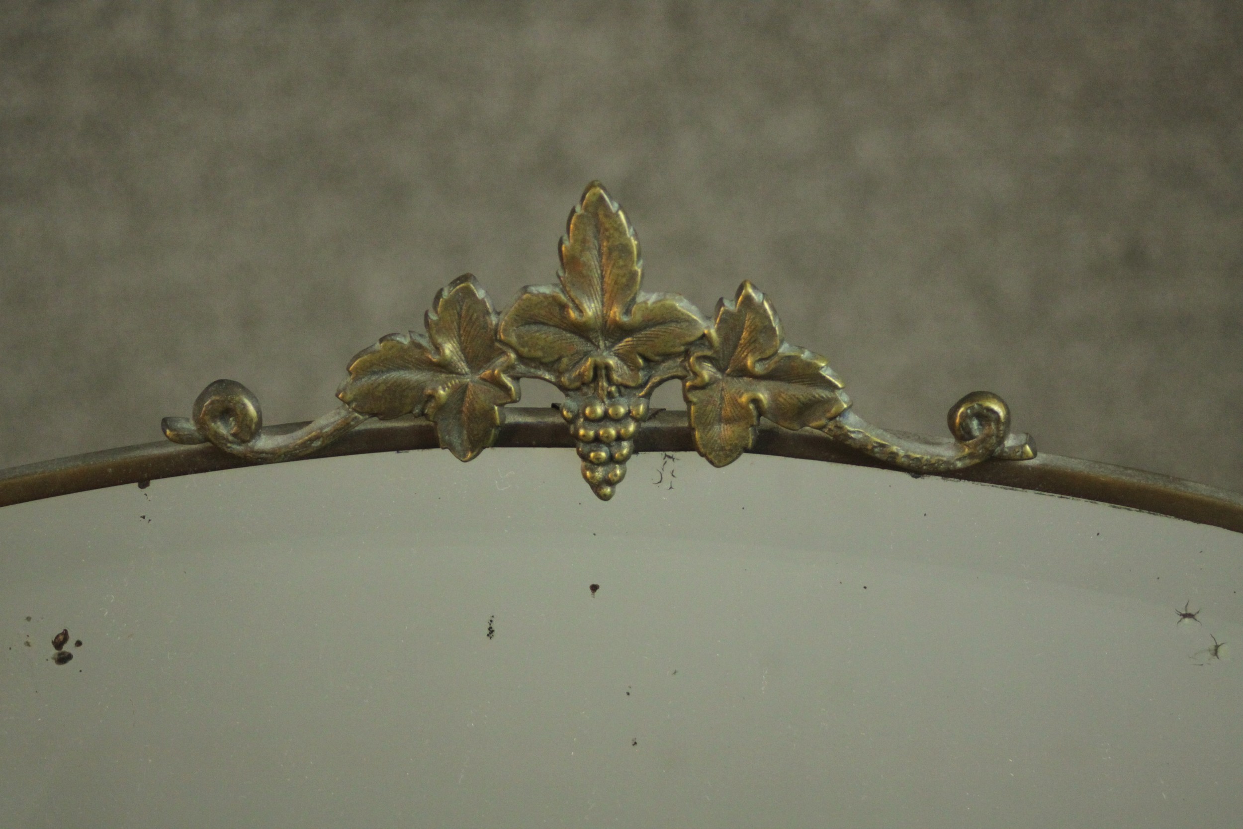 An early 20th century oval mirror in a brass frame and a vine crest. H.45 W.69cm. - Image 4 of 4