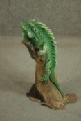 A hand painted clay figure of a green Iguana perched on a branch. H.53cm.