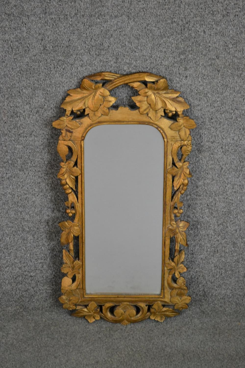 A carved giltwood mirror, the rectangular mirror plate with rounded corners in an ornately carved