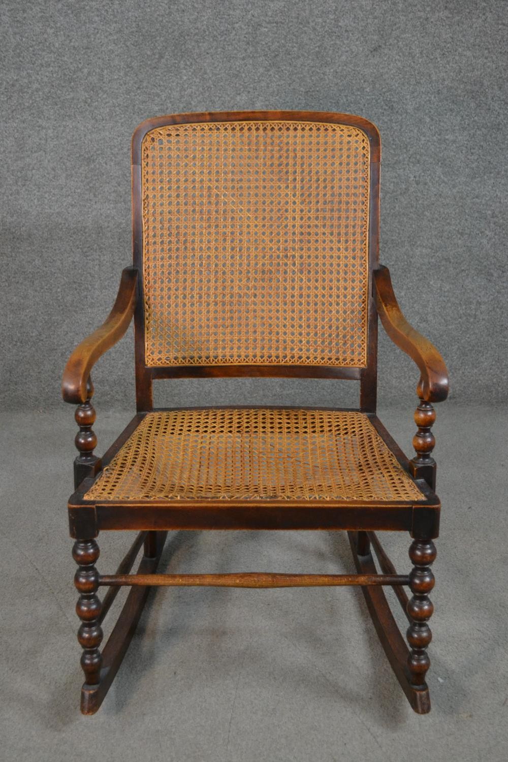 A circa 1900 stained beech rocking chair, with a caned back and seat, open arms, with bobbin