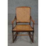 A circa 1900 stained beech rocking chair, with a caned back and seat, open arms, with bobbin