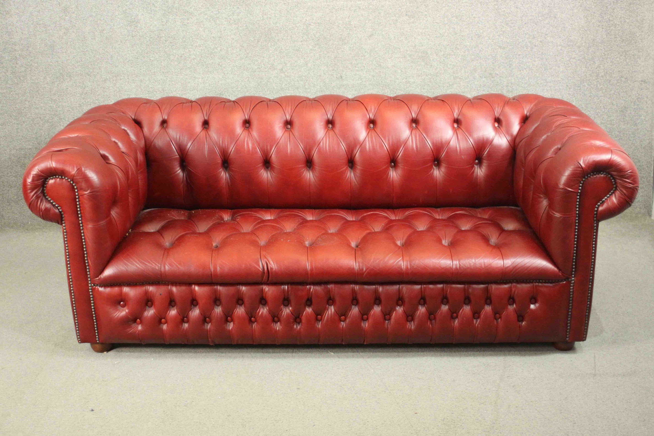 A red leather Chesterfield sofa, buttoned to the back, arms, seat, and front, on bun feet. H.75 W.