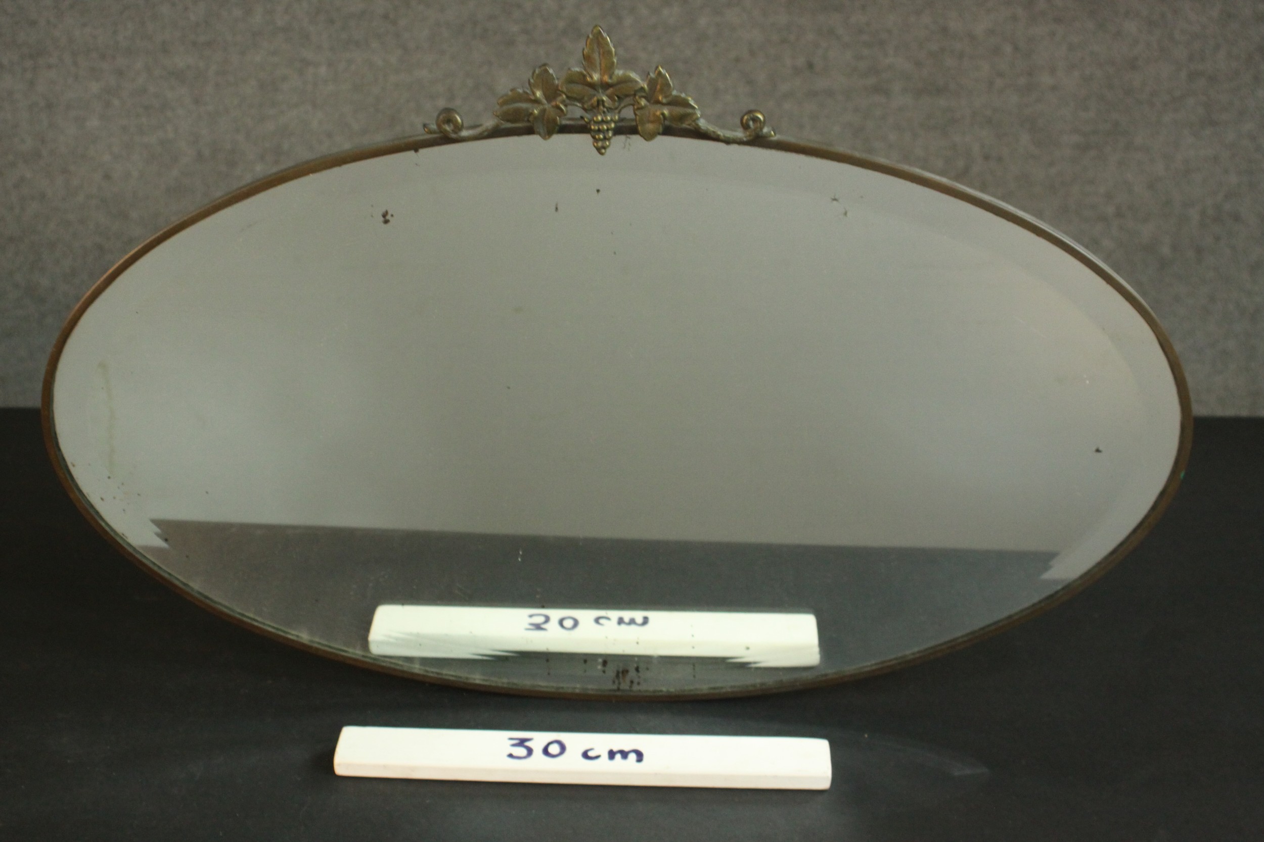 An early 20th century oval mirror in a brass frame and a vine crest. H.45 W.69cm. - Image 3 of 4