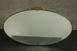 An early 20th century oval mirror in a brass frame and a vine crest. H.45 W.69cm.