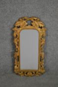 A carved giltwood mirror, the rectangular mirror plate with rounded corners in an ornately carved