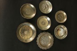 A collection of various silver and white metal dishes, including four with world coins, a hand