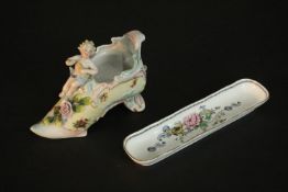 A 19th century hand painted porcelain slipper with relief cherub sitting upon it along with a