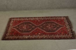 A Persian Shiraz rug with hooked lozenge medallions within stylised geometric borders. L.133 W.83cm.