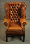 A child sized Georgian style wingback armchair in deep buttoned tan leather upholstery.