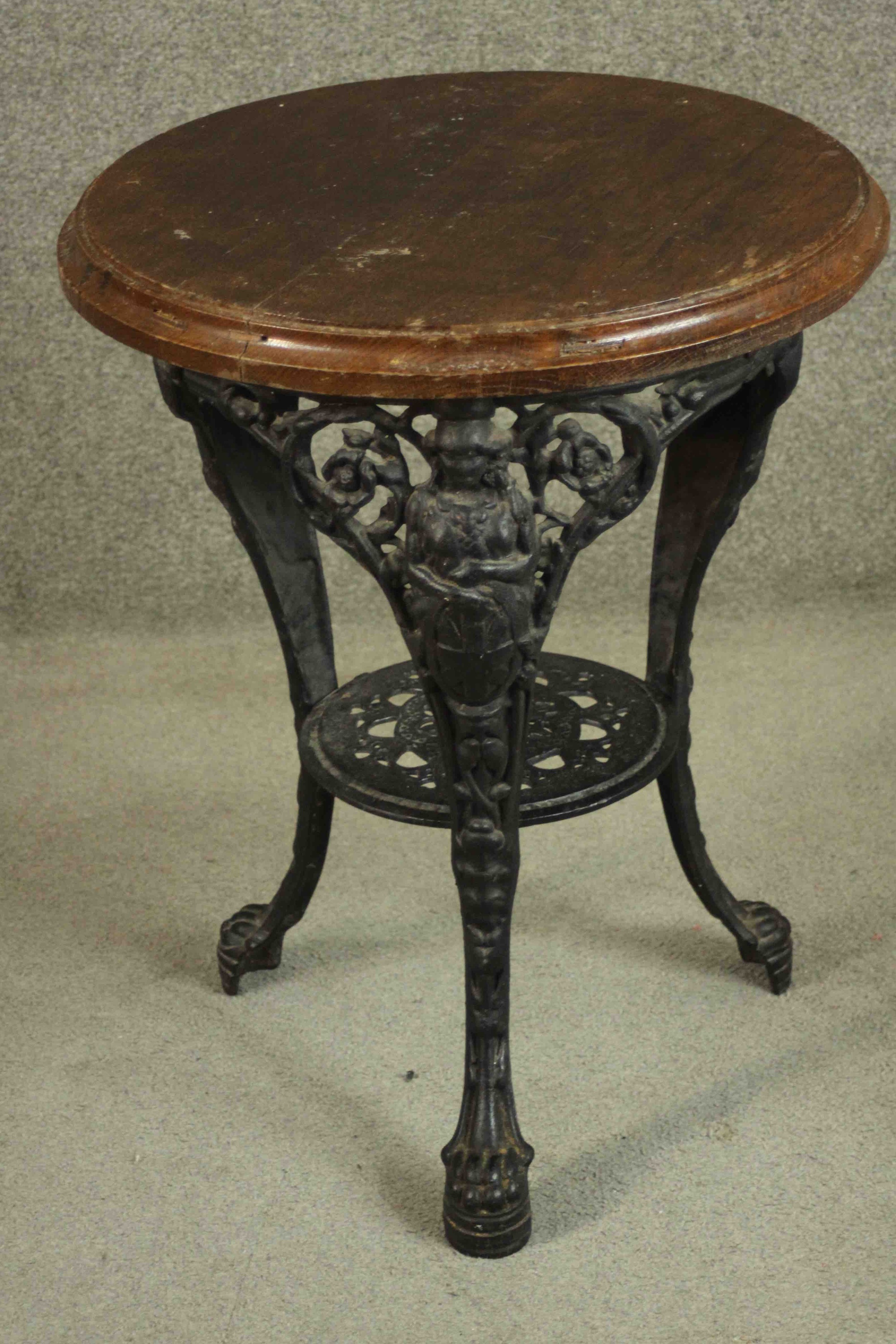 A black painted Victorian cast iron pub table with a circular oak top on three curved legs joined by