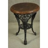 A black painted Victorian cast iron pub table with a circular oak top on three curved legs joined by