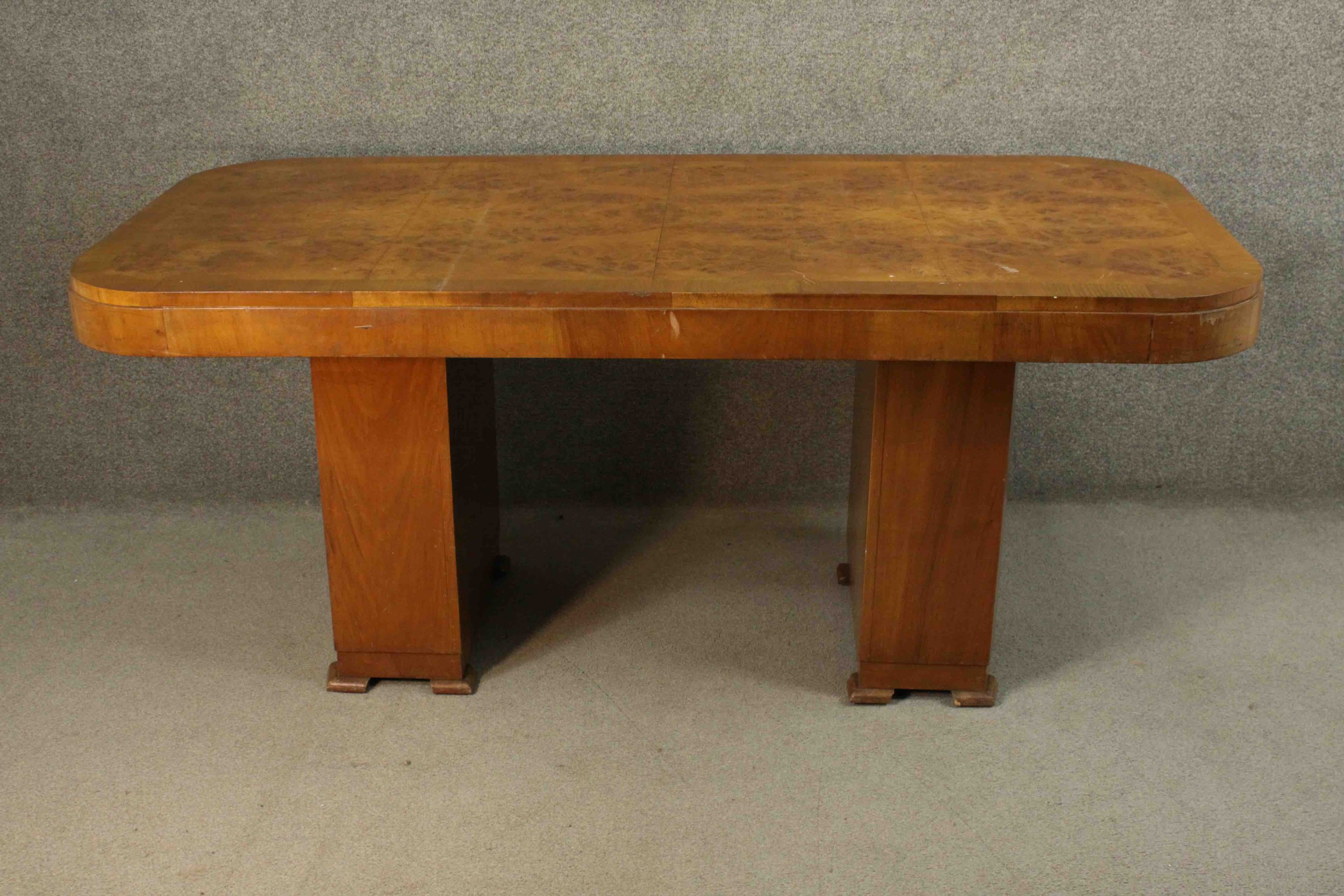 An Art Deco burr walnut and crossbanded dining table with rounded rectangular top on twin pillar