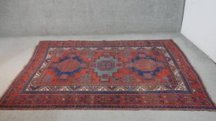 A hand woven Persian Kurdish carpet with geometric medallions on a madder field within stylised