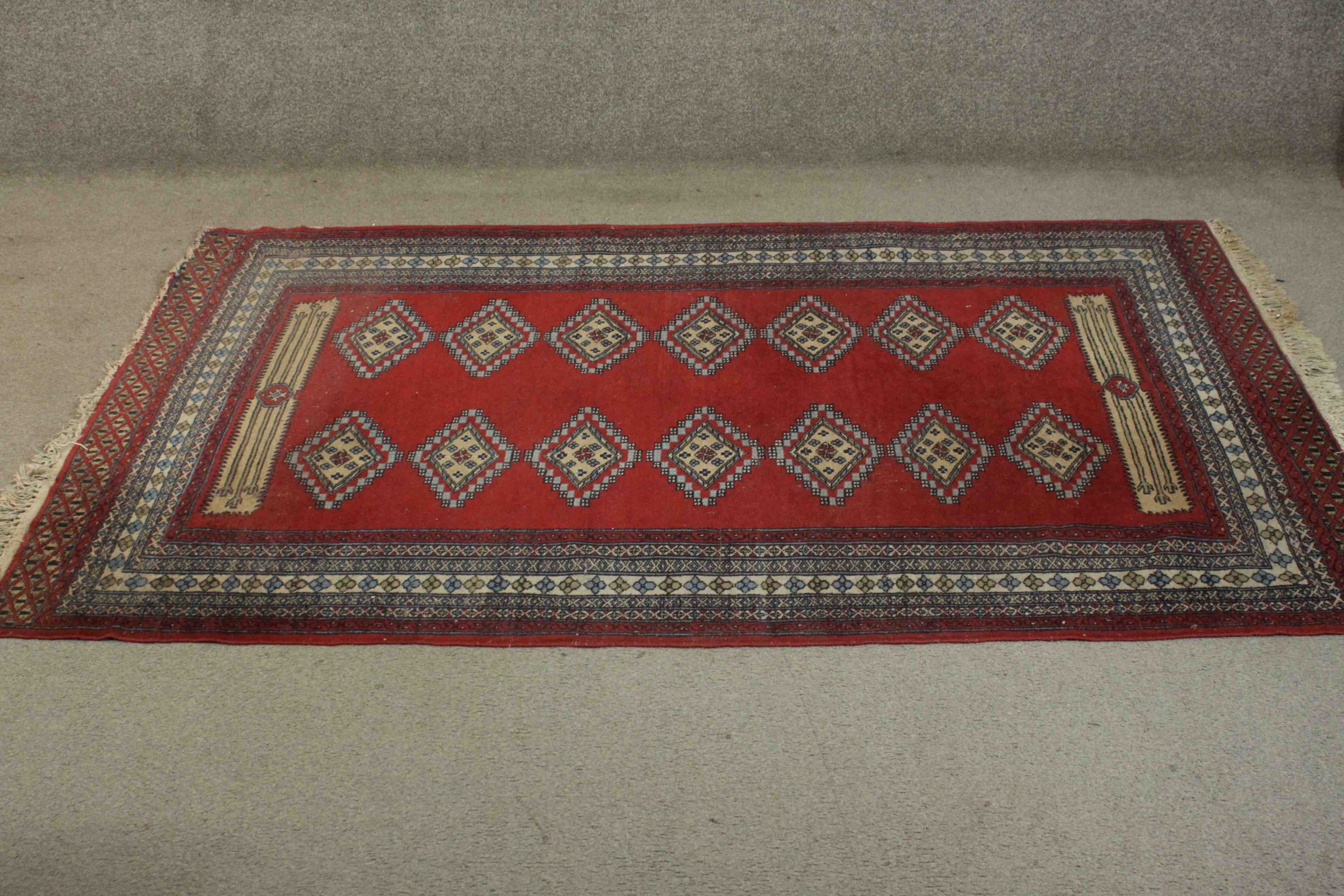 A Pakistan Bokhara with repeating diamond motifs on a burgundy field within stylised flowerhead
