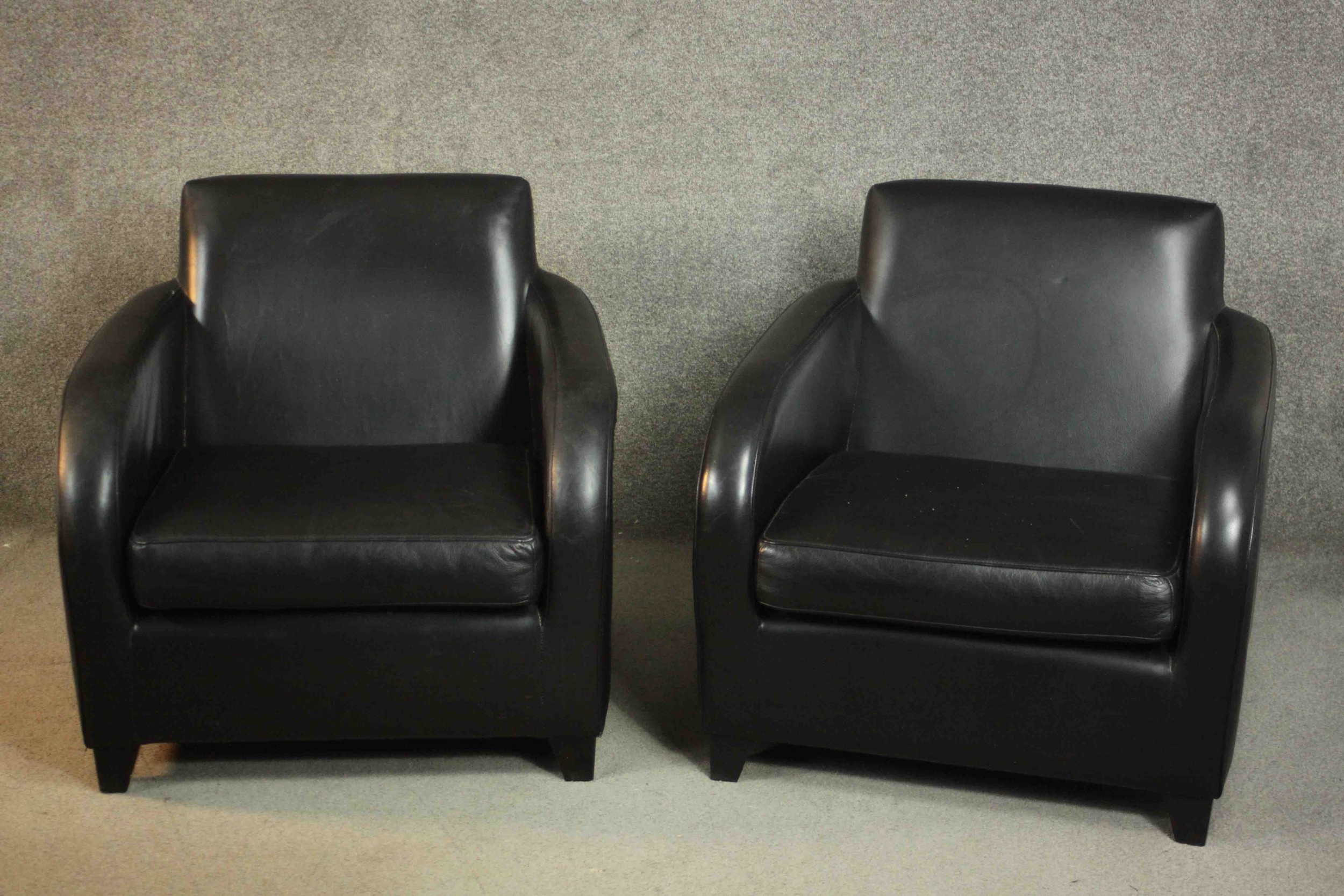 A pair of contemporary black leather armchairs, on tapering block feet.