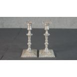 A pair of Edwardian sterling silver weighted repousse design candlesticks on square bases. The