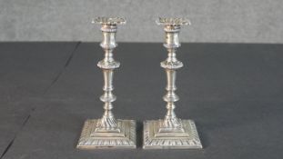 A pair of Edwardian sterling silver weighted repousse design candlesticks on square bases. The