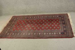 A Pakistan Bokhara rug with repeating hooked medallion motif across a burgundy field. L.190 W.125cm.
