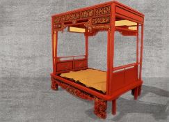 A Chinese red lacquered four poster 'opium' bed, with carved parcel gilt panels, with ebonised