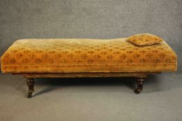 A Victorian daybed or doctor's examining bed, upholstered in a patterned mustard fabric with a loose