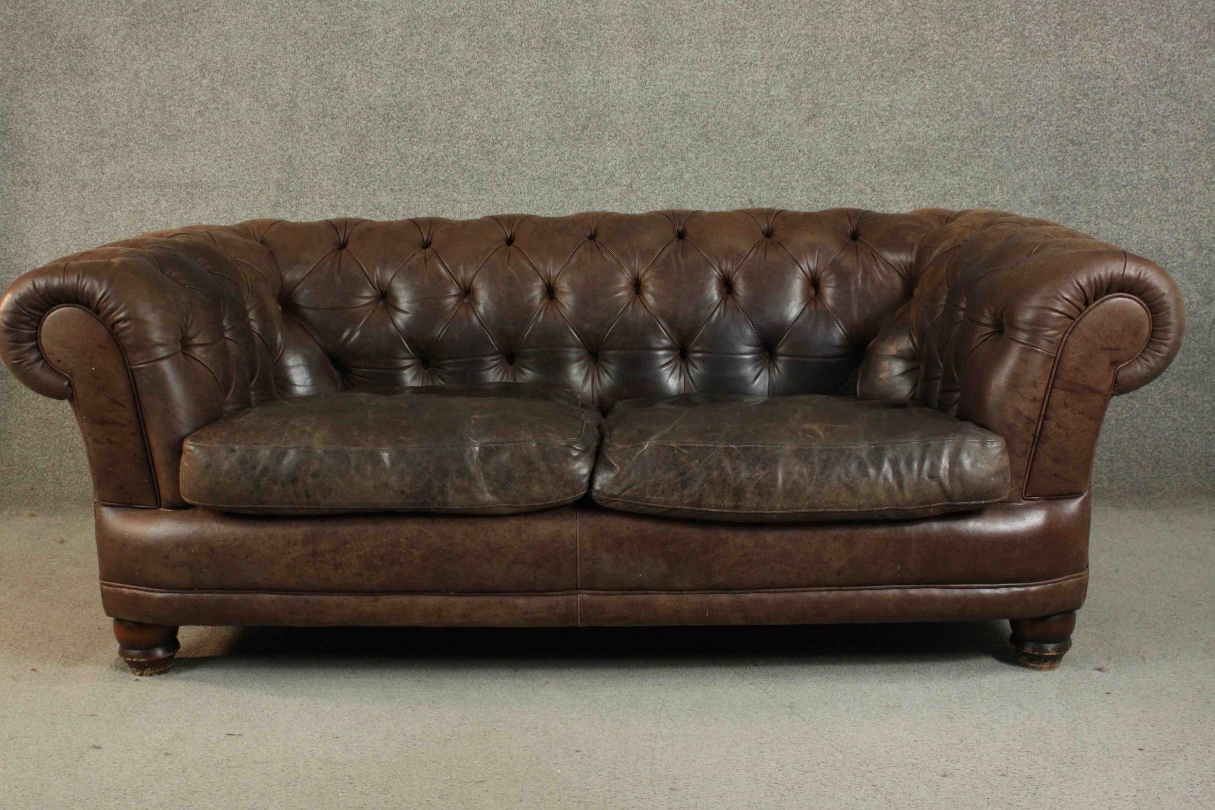 A contemporary brown leather Chesterfield sofa, with buttoned scrolling arms and back, on turned