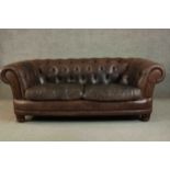 A contemporary brown leather Chesterfield sofa, with buttoned scrolling arms and back, on turned