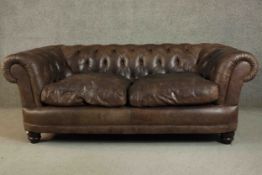 A contemporary brown leather Chesterfield sofa, with buttoned scrolling arms and back, on turned