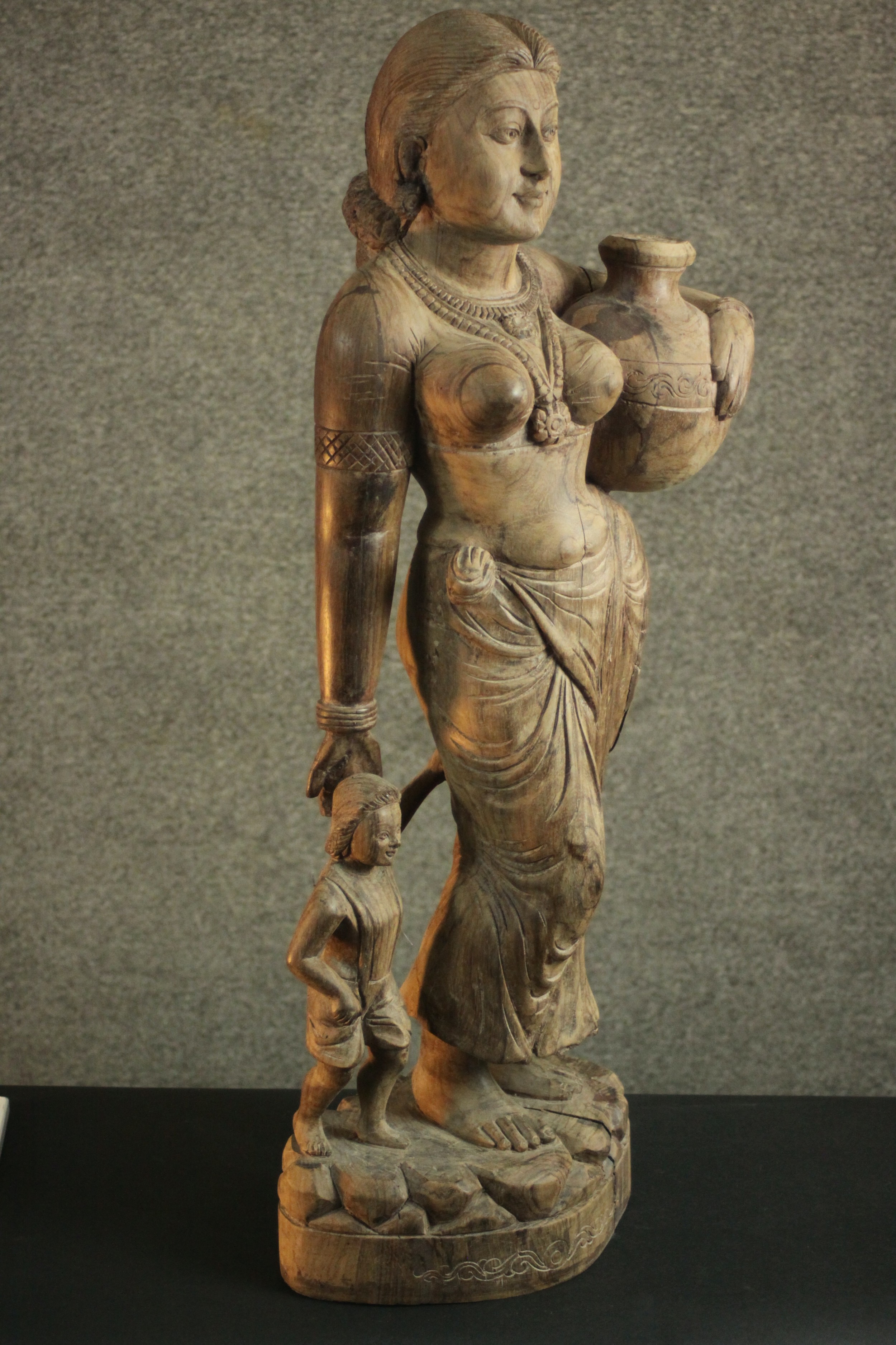A 20th century carved figure of a woman holding her child's hand and carrying a water vessel. H.78