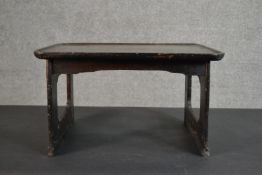 A small ebonised pine table, possibly Korean, with a dished rectangular top on pierced end supports.