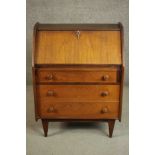 A circa 1960s teak bureau, the fall front enclosing pigeonholes above three long graduated drawers