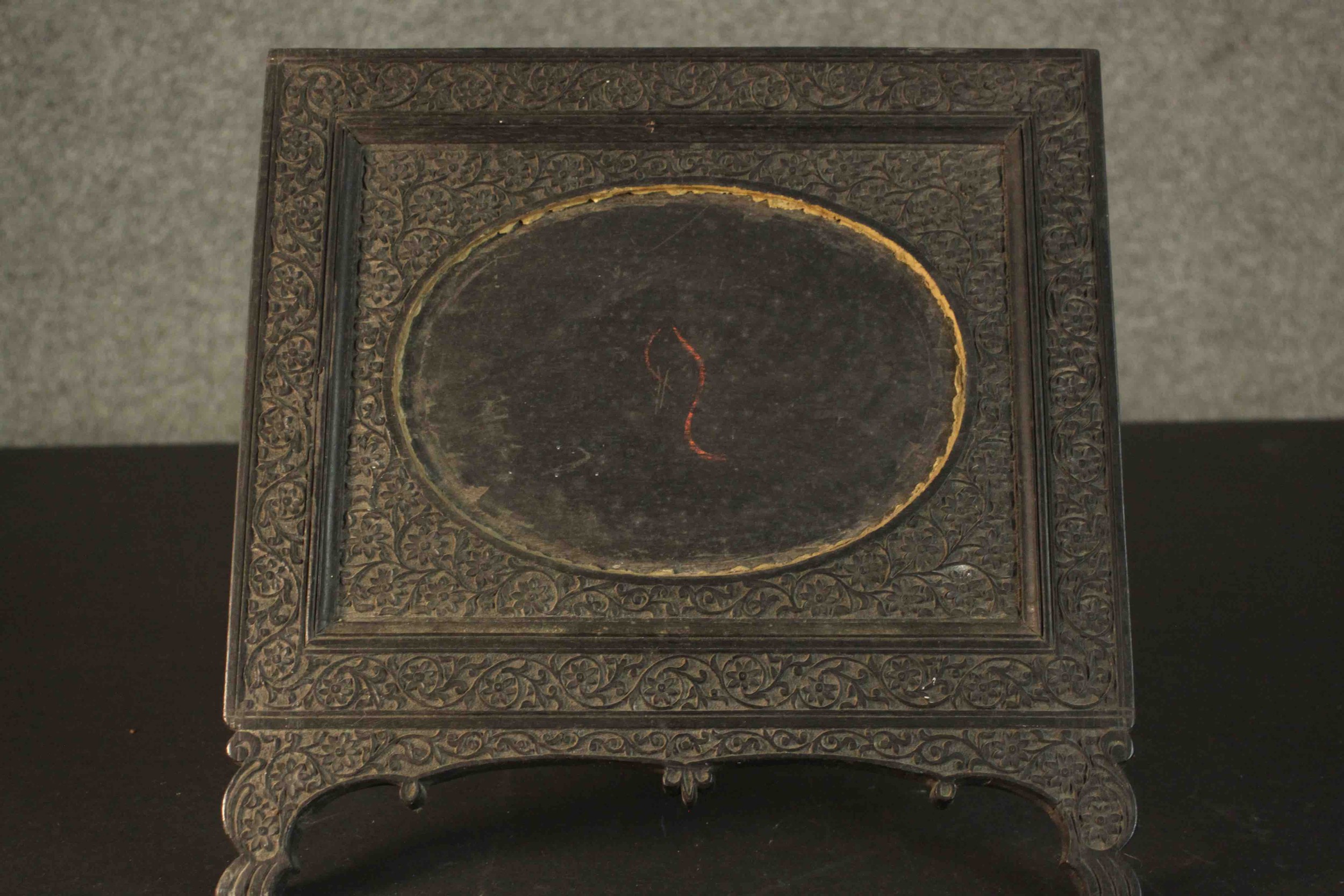 An Anglo-Indian ebonised carved easel picture frame with floral design and oval cartouche to centre.