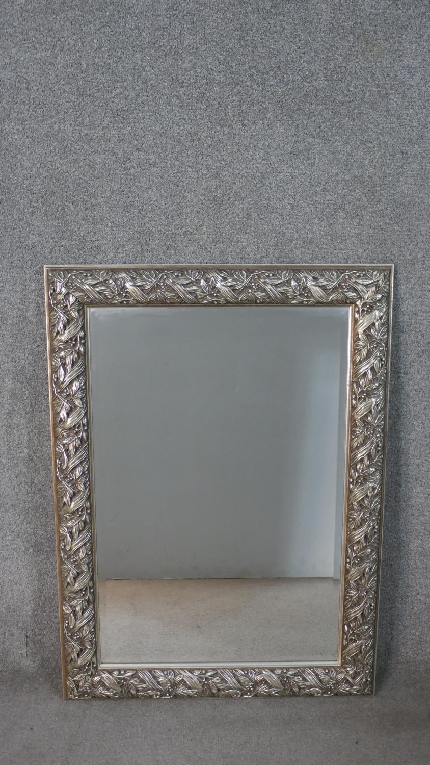 A silver painted moulded foliate and ribbon design wall mirror. H.107 W.78cm