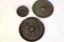 Three Meji period Japanese bronze mirrors, one decorated with dragons and figures around a central